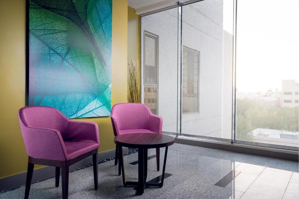A bright lounge corner with plum armchairs and a floor-to-ceiling window